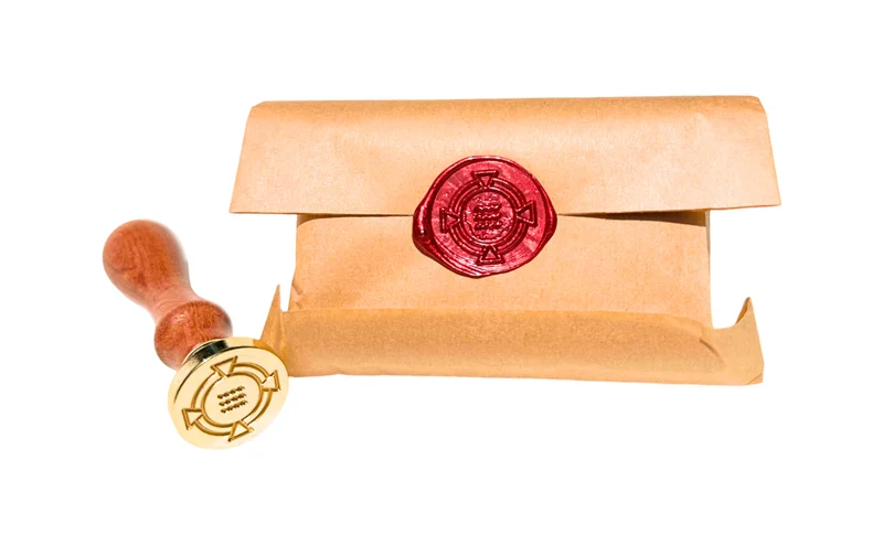 A bar of Order Soap wrapped in kraft paper and hand-sealed in red wax with the symbol of ORDER, beside the brass seal