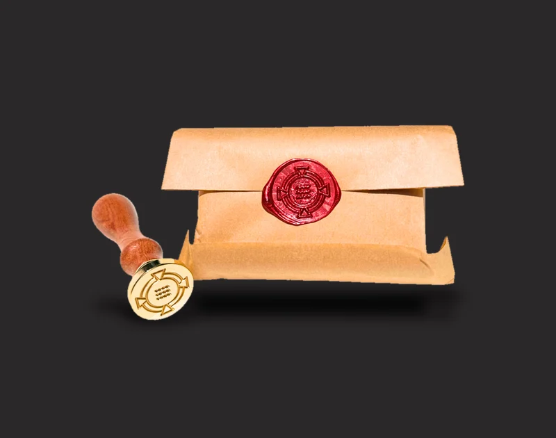 A bar of Order Soap wrapped in kraft paper and hand sealed in red wax with the symbol of ORDER, beside the brass seal